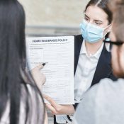 A woman in a mask holding papers and talking to people.